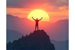 Eine Person steht auf einem Berggipfel und blickt auf einen Sonnenaufgang. Symbolisiert Zielerreichung und Selbstmotivation.